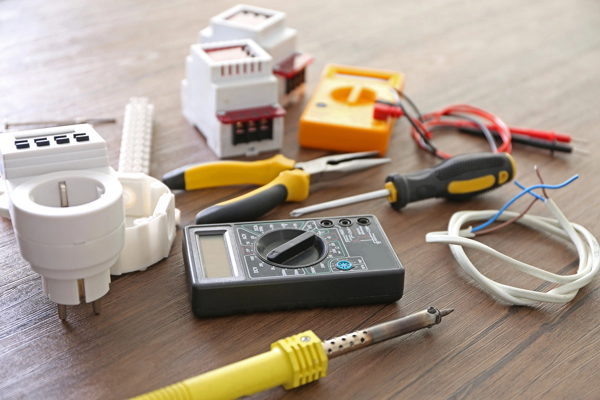 Ensemble d'outils et de matériel électrique, incluant des pinces, des fils et un multimètre, sur une table.